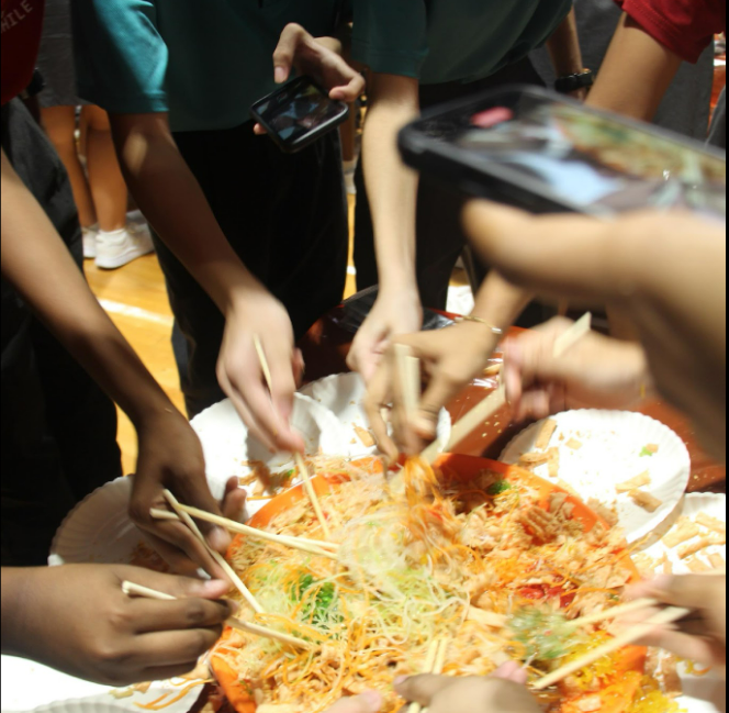 Multiple hands using chopsticks to toss a colorful shredded salad dish together around a shared plate.